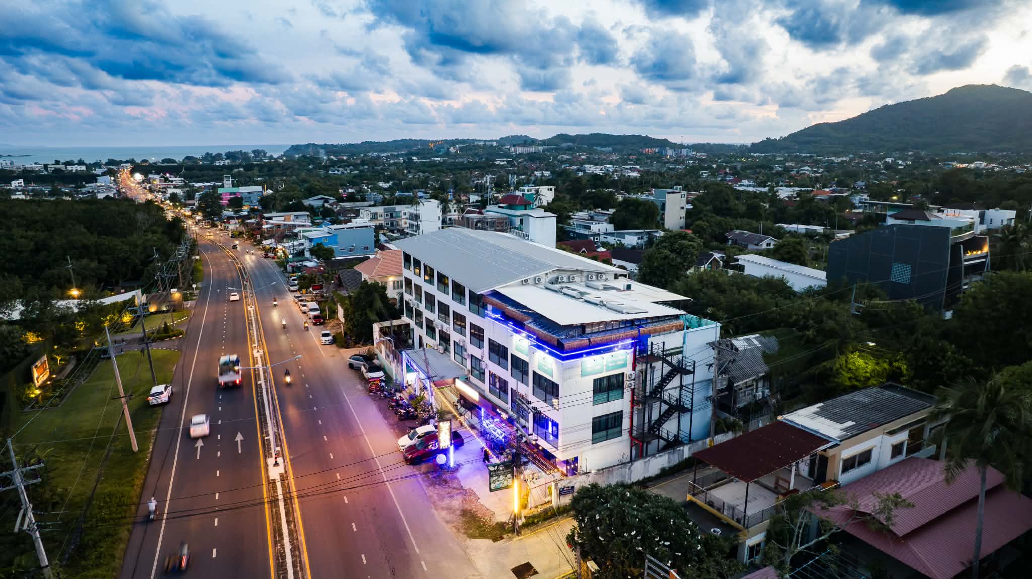 De Blue Sea Rawai Hotel lit at dusk above Wiset Road, Rawai